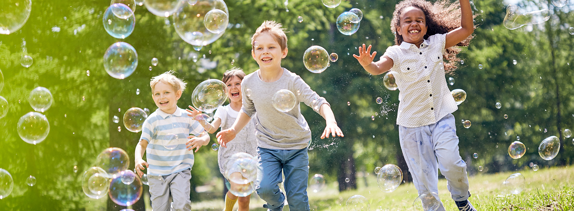 Three children playing with bubbles in a field.