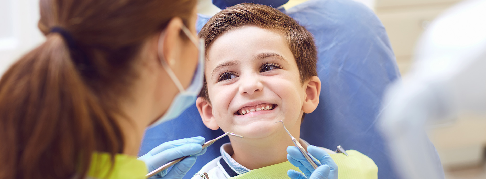 A young boy is being examined by a dental professional, sitting in a dentist s chair with a smiling expression.