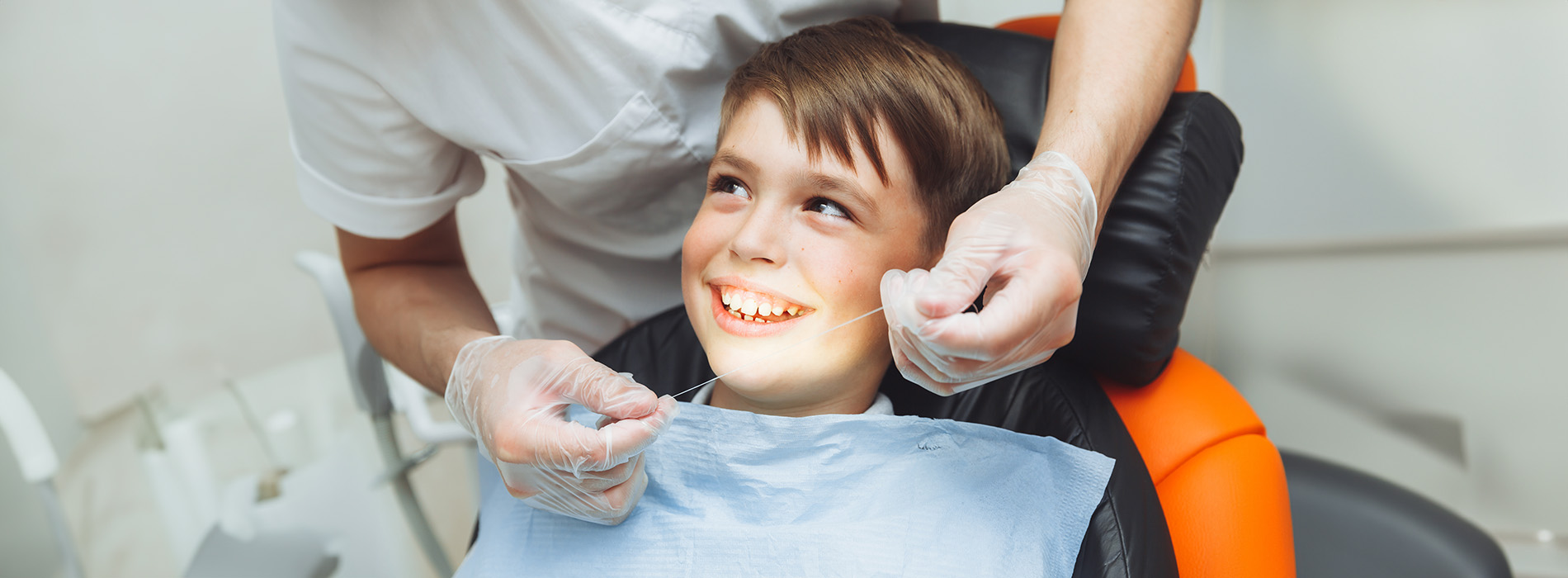 A dental hygienist assisting a child in a dental chair during a teeth cleaning appointment.