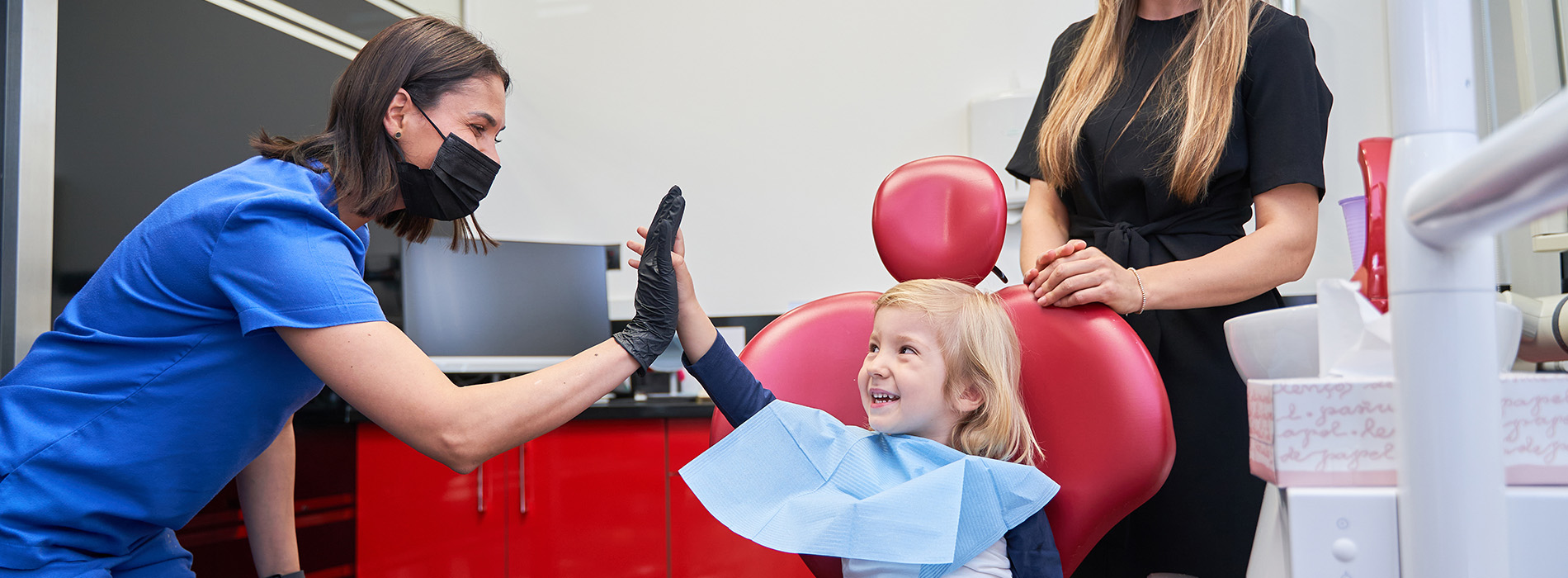 A dental hygienist giving a child a check-up while a woman looks on.