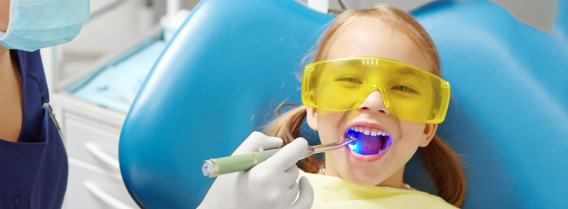 A child in a dental chair receiving treatment, with a dental professional in the background.