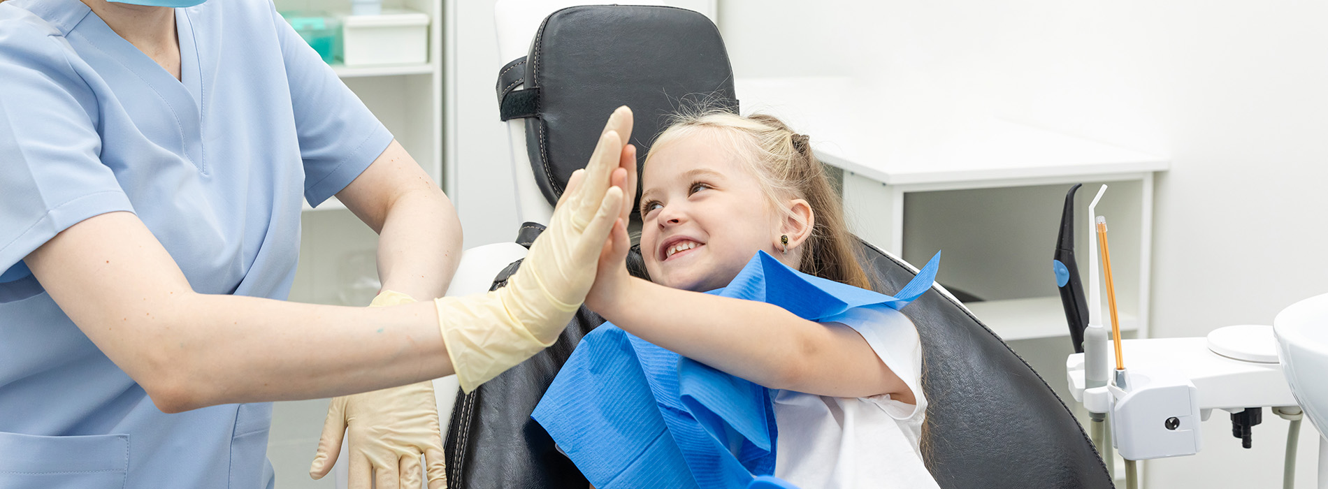 A young child sitting in a dental chair, receiving attention from a dental professional.