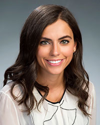 The image is a portrait of a woman with a smile, wearing a white top and posing for the photograph.